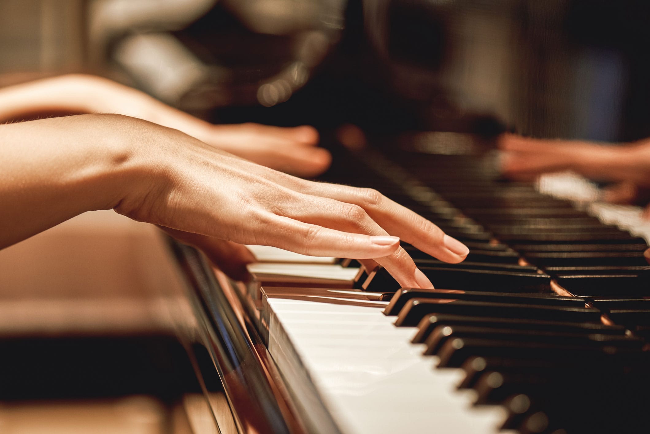 Close-up of hands playing the keys on a polished piano.