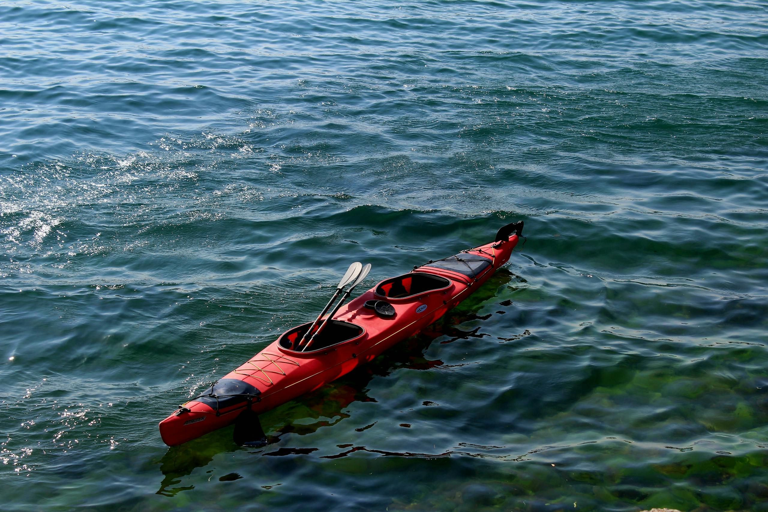 Red tandem kayak floating on clear greenish-blue water with two paddles resting across the cockpit openings.